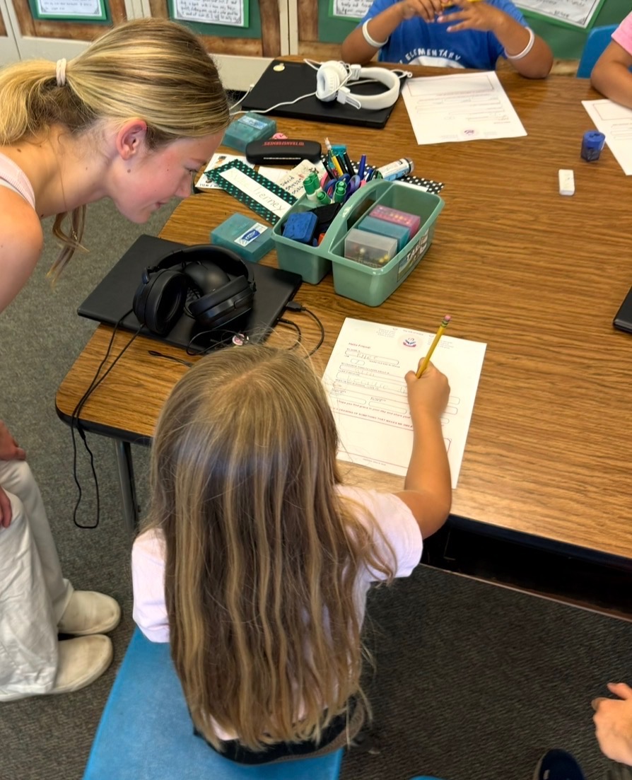 Grace leaning in to help a student with her letter
