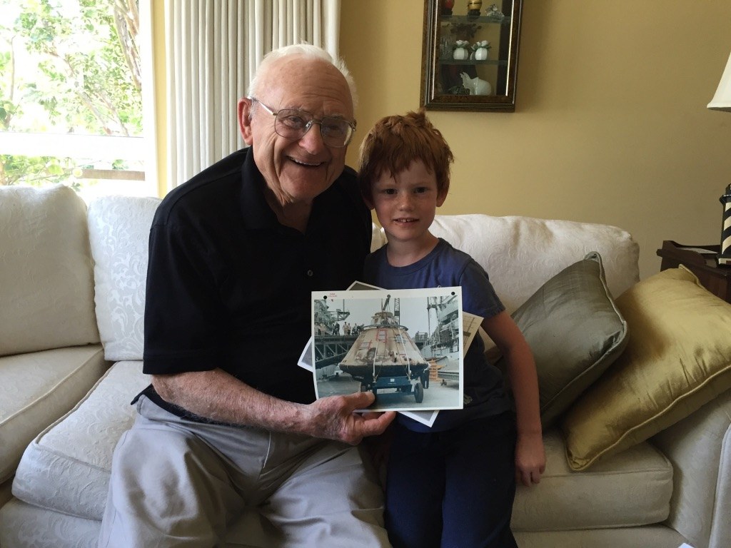 Mr. Peck smiling on his couch with Grace's little brother, holding up one of his old photos
